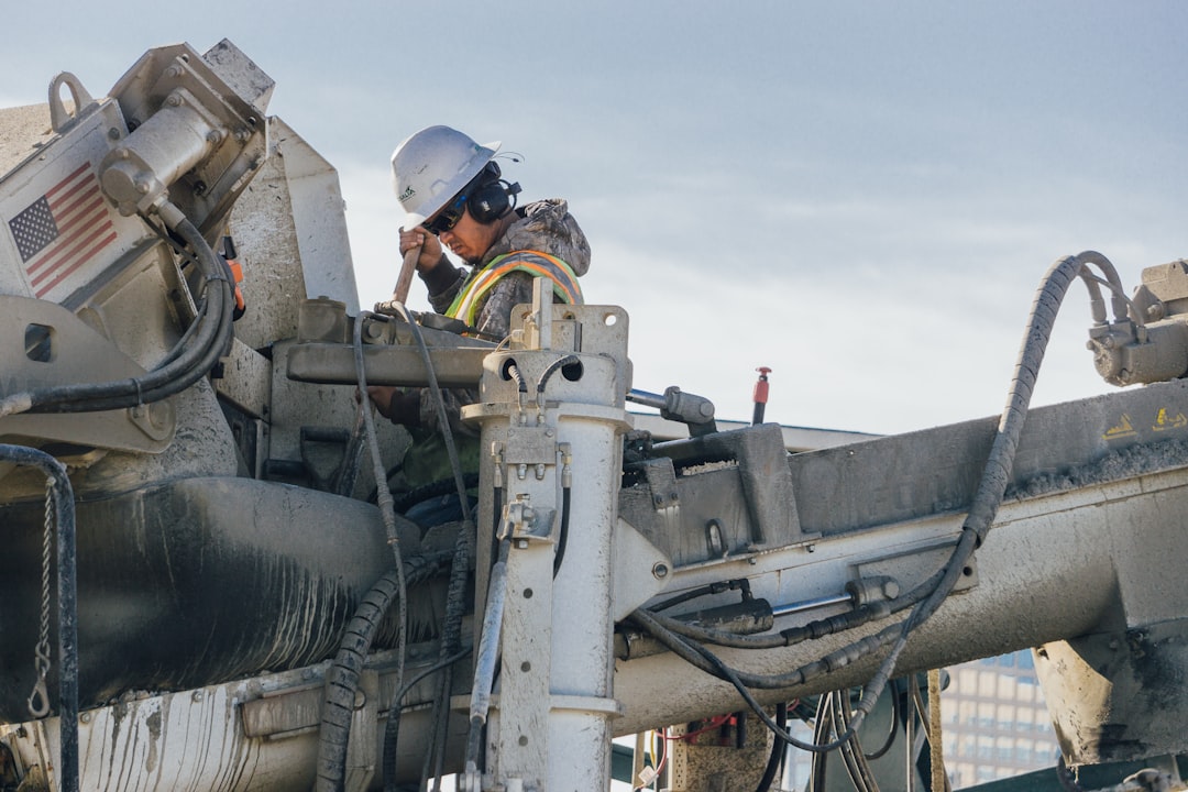 Construction worker in safety helmet, eye protection and hearing protection inspecting heavy equipment